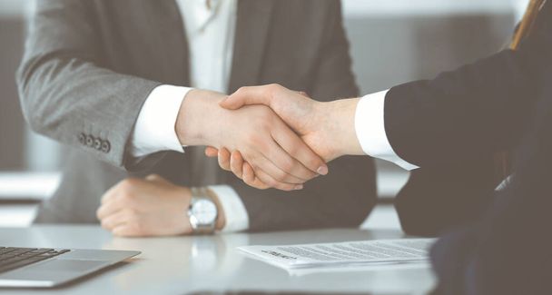 Unknown businessman shaking hands with his colleague or partner above the glass desk in modern office, close-up. Business people group at meeting - Photo, image