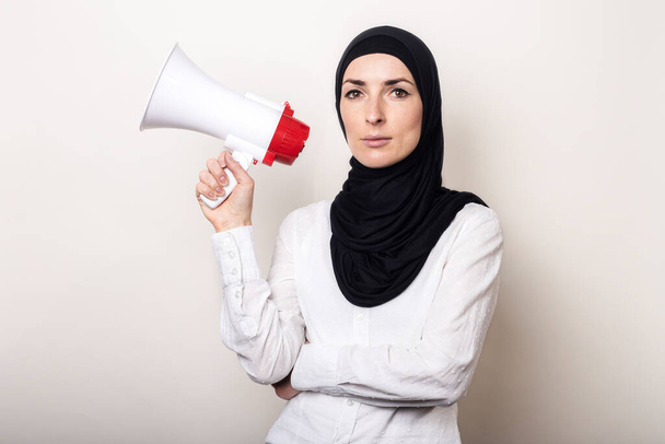 Мусульманська молода жінка в Хіджабі тримає мегафон в руках на світлому тлі. Банер. - Фото, зображення