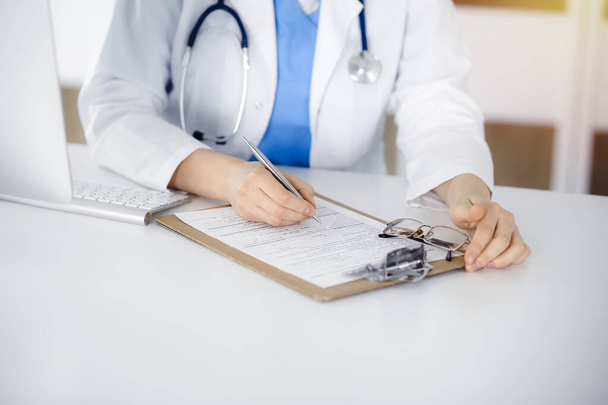Femme-médecin inconnue au travail remplissant le formulaire d'historique de médicaments dans une clinique ensoleillée, gros plan - Photo, image