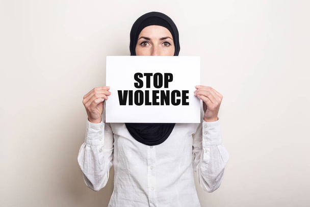 Jovem muçulmana em hijab cobre o rosto com uma bandeira com o texto STOP VIOLENCE. - Foto, Imagem