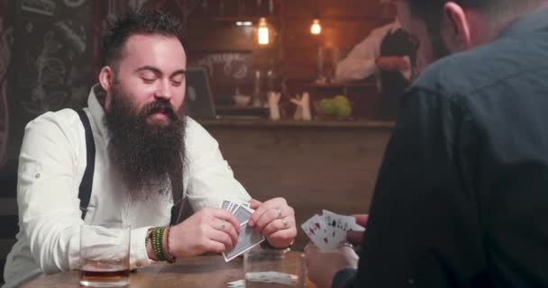 Positiver junger bärtiger Mann mit seinem Freund in einer Kneipe beim Kartenspiel - Filmmaterial, Video