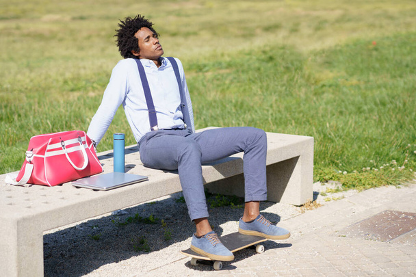 Zwarte man met afro haar neemt een koffiepauze zittend op een bankje in het park. - Foto, afbeelding