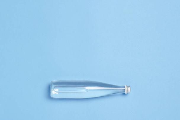 Botella de vidrio con agua clara sobre fondo azul. Concepto de salud y belleza, equilibrio hídrico, sed, calor, verano. Piso tendido, vista superior. - Foto, Imagen