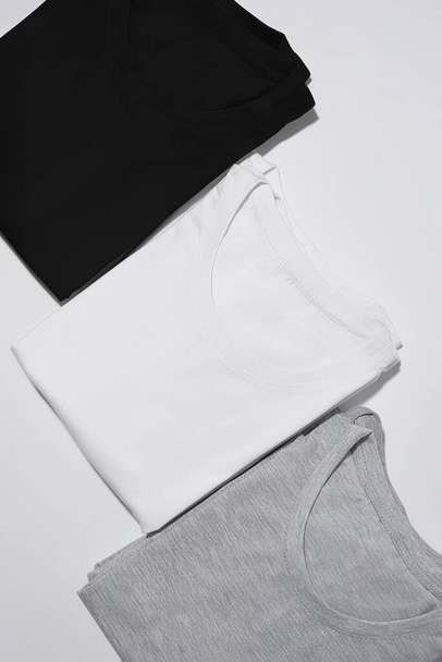 Tres camisetas monocromáticas plegadas gris, blanco y negro aisladas sobre fondo gris - Foto, Imagen
