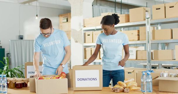 Social help. Volunteers man and woman collecting food donations in warehouse. Social workers putting products in parcel. Charity, Donating, Donate. Volunteering activity concept, humanitarian help - Fotografie, Obrázek