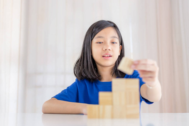Dziewczyna bawiąca się drewnianymi kostkami zabawki edukacyjne w salonie w domu, azjatyckie dziecko bawiące się z projektantem bloków zabawek na stole, Dzieci koncepcji uczenia się. - Zdjęcie, obraz