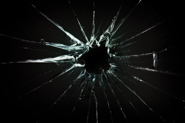 Das Loch im zerbrochenen und rissigen Glas, Nahaufnahme auf dunklem Hintergrund - Foto, Bild