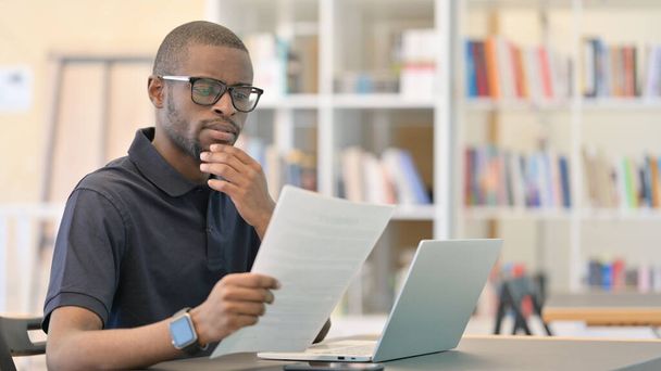 Молодий африканський чоловік читає документи, папери в бібліотеці
 - Фото, зображення