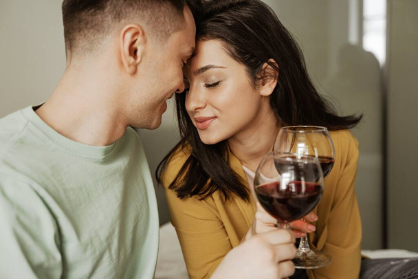 Preciosa pareja con copas de vino tiene una cena romántica en casa. Familia joven feliz se mudó a nuevo apartamento - Foto, imagen