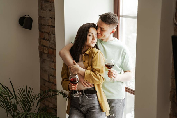 Lovely couple with glasses of wine at home, romantic vibes. Happy young family moved to new apartment - Fotoğraf, Görsel