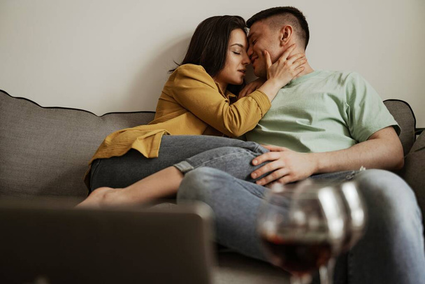 Прекрасная пара целуется с романтическими чувствами, сидя на диване в гостиной. Счастливая семья переезжает в новую квартиру - Фото, изображение