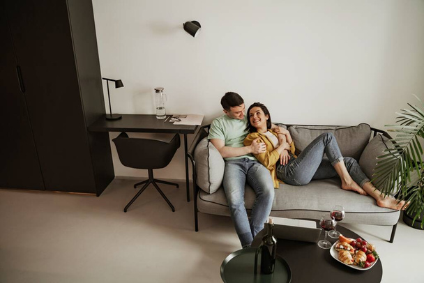 Ihana nuori pari osoittaa romanttinen tunne toisilleen istuu sohvalla olohuoneessa. Onnellinen perhe muuttamassa uuteen asuntoon - Valokuva, kuva