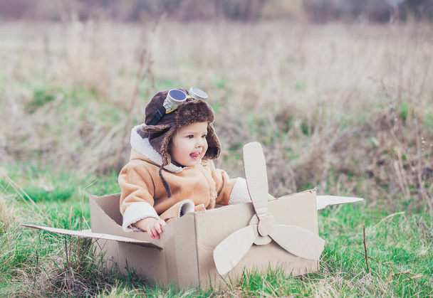 Очаровательный ребенок в самодельном картонном самолете воображает, что он летает - Фото, изображение