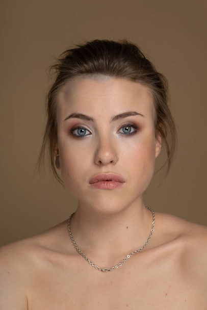 Portrait of a young alternative model with heterochromia, short hair, good makeup, eyeliner, pale skin, piercings. Looks straight ahead. Feminism and Empowerment. Beauty studio shot beige background - Foto, immagini