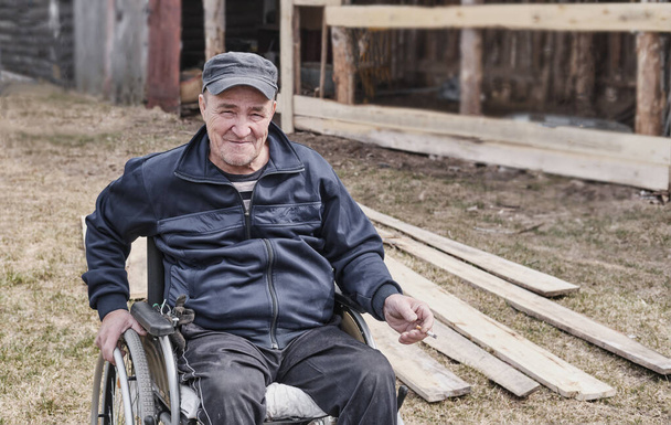 Старший чоловік у інвалідному візку у дворі свого будинку
 - Фото, зображення