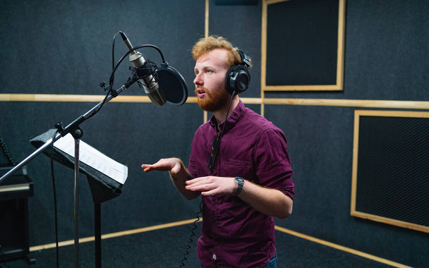 Expressive bearded man with curly ginger hair in headphones at recording studio - Fotoğraf, Görsel