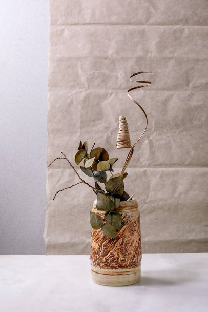 Dry flowers, eucalyptus and twigs branch in brown ceramic vase on white marble table with gray wall behind. Copy space. - Foto, afbeelding