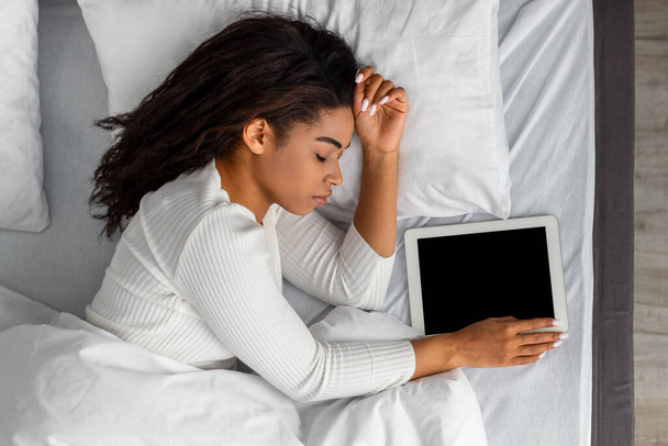 Schwarze Frau liegt schlafend im Bett und hält Tablette in der Hand - Foto, Bild