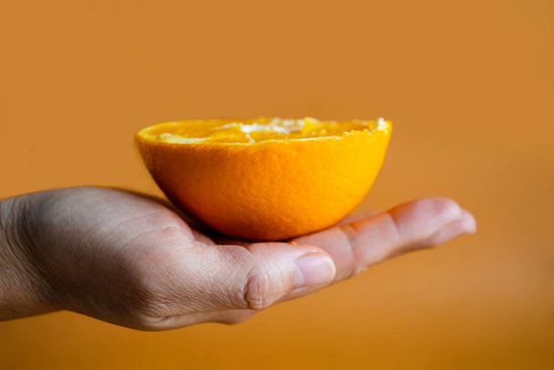 Mains de femme tenant des moitiés d'orange sur fond jaune orange. - Photo, image