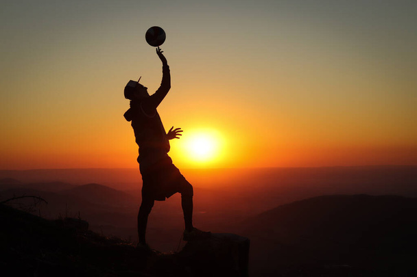 extraligový volejbalista stojí na pařezu na vrcholu hory a při západu slunce si hraje s volejbalovým míčem v jedné ruce. Silueta v noci. - Fotografie, Obrázek