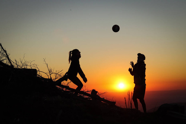 Два молодых спортсмена мужчины и женщины в возрасте 25-30 лет играют в волейбол на вершине горы на закате. Спортивный момент. Активная жизнь. Проход над головой. Волейбольный удар, удар, удар. - Фото, изображение
