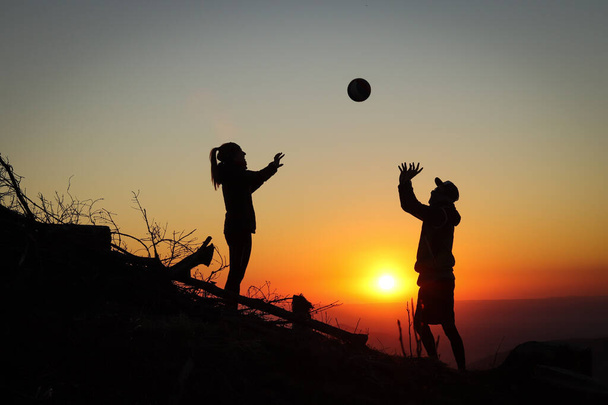 Молодая волейбольная пара наслаждается вершиной розовой горы с мячом на закате. Силуэты женщины и игрока, щипающих свои пальцы мячом. Волейбольный удар, удар. Пропуск. - Фото, изображение
