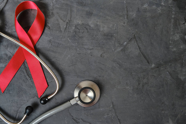 Red ribbon symbol of AIDS, drug abuse problem, stethoscope on concrete texture background - Foto, immagini