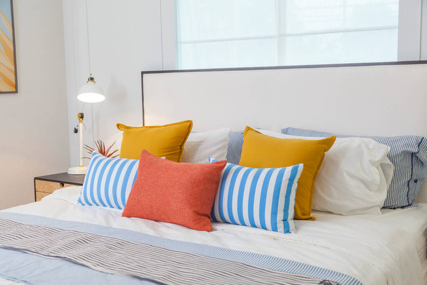 Keltainen, oranssi ja sininen tyyny asetus sängyllä valkoinen kodikas makuuhuone. - Valokuva, kuva