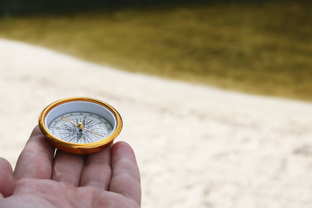 Oude klassieke navigatie kompas in de hand op natuurlijke achtergrond als symbool van het toerisme met kompas, reizen met kompas en outdoor activiteiten met kompas - Foto, afbeelding