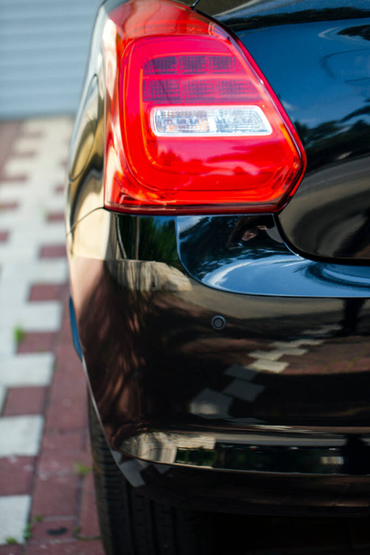 Carro farol traseiro esquerdo perto. indicador de volta vermelho de um automóvel de luxo preto em um estacionamento. Luzes traseiras de carro moderno que brilham brilhantemente ao ar livre. Foco seletivo - Foto, Imagem
