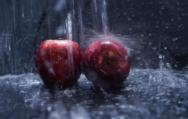 Δύο κόκκινα μήλα βρεγμένα από νερό πιτσιλίζουν, θολό φως γύρω - Φωτογραφία, εικόνα