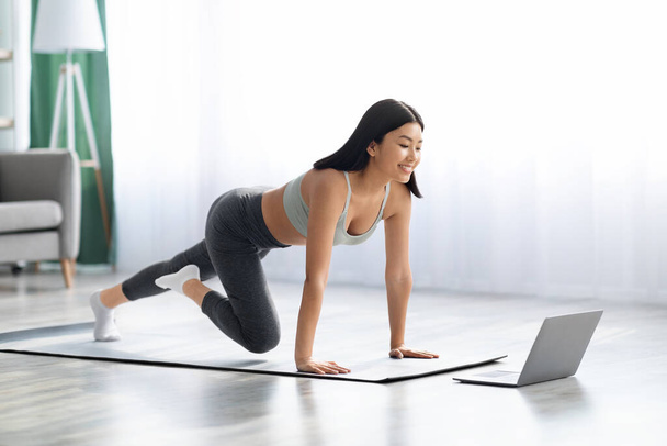 Fitness Online. Feliz joven asiática mujer haciendo deportes en casa con el ordenador portátil - Foto, Imagen