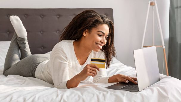 Ευτυχισμένη μαύρη γυναίκα που κρατάει χρεωστική πιστωτική κάρτα, χρησιμοποιώντας φορητό υπολογιστή - Φωτογραφία, εικόνα