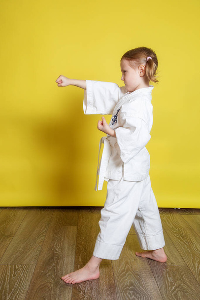 Portrait Of 5 year old caucasian Girl in kimono Practicing Karate Against yellow Background at home - Zdjęcie, obraz
