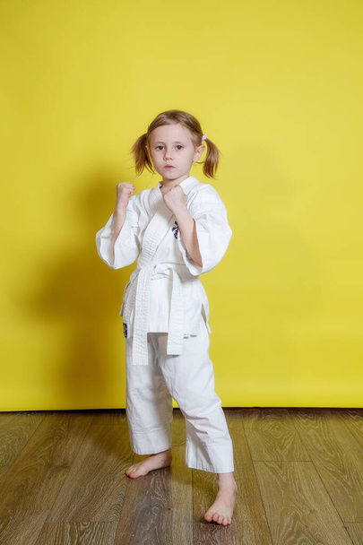 Portrait Of 5 year old caucasian Girl in kimono Practicing Karate Against yellow Background at home - Foto, afbeelding