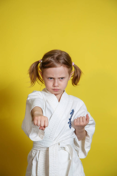 Portrait Of 5 year old caucasian Girl in kimono Practicing Karate Against yellow Background at home - Photo, Image