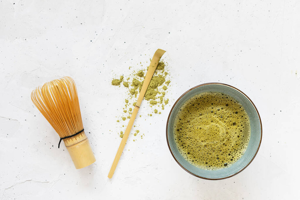 Té verde matcha en tazón, cuchara con polvo de té seco disperso y batidor sobre fondo blanco - Foto, imagen