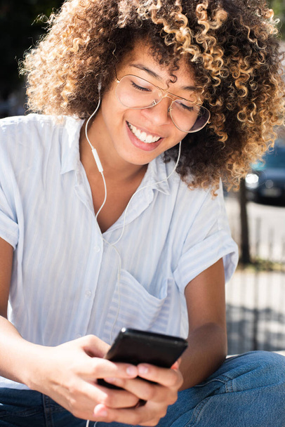 Primer plano retrato feliz joven afroamericana escuchando música con teléfono móvil y auriculares - Foto, Imagen