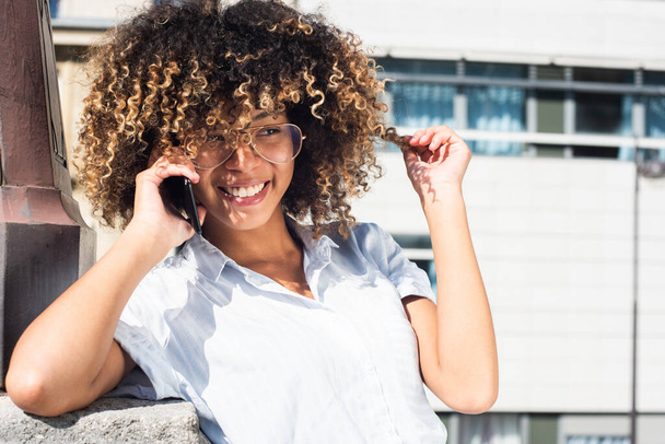 Gros plan portrait horizontal souriant jeune femme afro-américaine parlant avec téléphone portable à l'extérieur - Photo, image