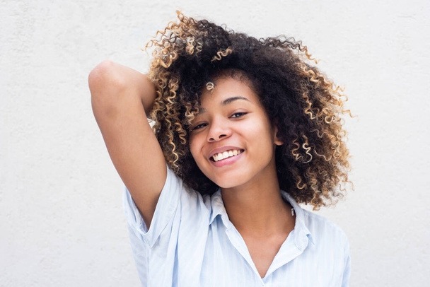 Close up poziome portret uśmiechnięty młody Afroamerykanin kobieta z ręką we włosach przez białą ścianę - Zdjęcie, obraz