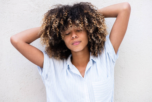 Portret afrikaanse Amerikaanse jonge vrouw met gesloten ogen en handen achter hoofd tegen witte achtergrond - Foto, afbeelding