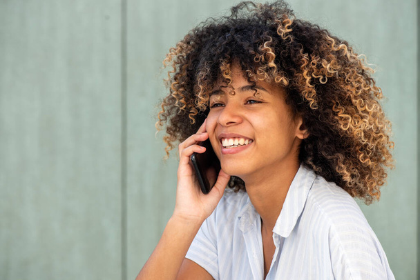 Gros plan portrait jeune femme afro-américaine souriante tout en parlant avec téléphone portable  - Photo, image