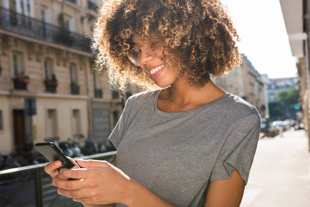 Portret uśmiechnięty czarny dziewczyna patrząc na telefon komórkowy w mieście - Zdjęcie, obraz