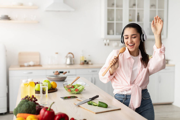 Portrait of smiling young woman singing and dancing in kitchen - Foto, Imagen