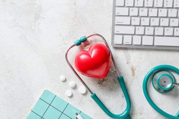 Modern stethoscope with heart and computer keyboard on light background - Fotó, kép