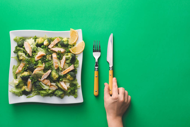 Жіноча рука і тарілка смачного салату зі свіжими овочами на кольоровому фоні
 - Фото, зображення