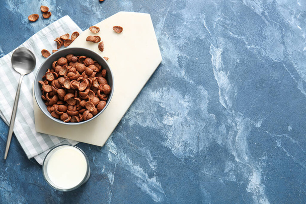 Bowl with chocolate cornflakes and glass of milk on color background - Zdjęcie, obraz