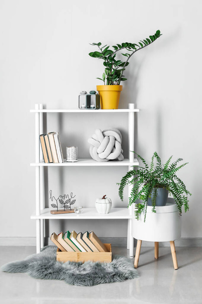 Moderne Regaleinheit mit Büchern und Zimmerpflanzen nahe weißer Wand im Zimmer - Foto, Bild