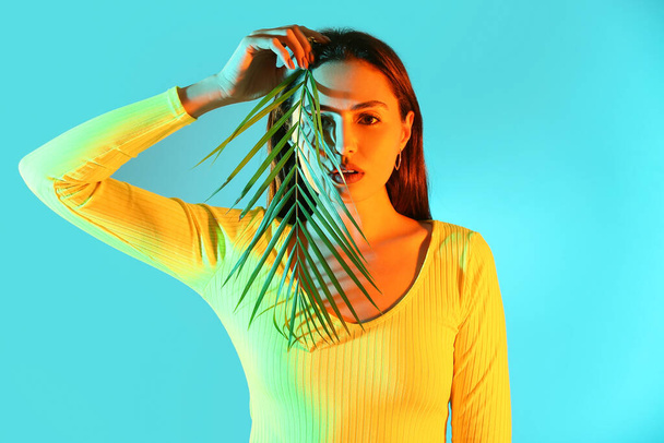 Retrato tonificado de una hermosa joven con hoja tropical sobre fondo de color - Foto, Imagen