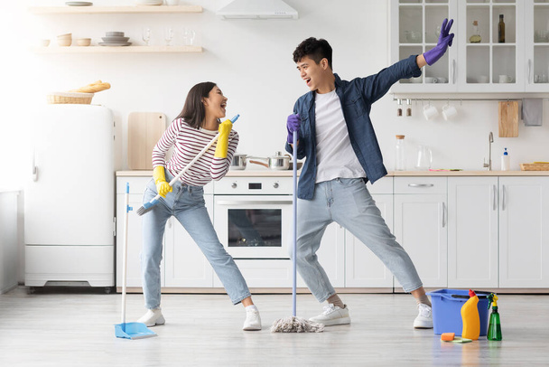 Funny asian couple singing songs while cleaning kitchen, copy space - Fotografie, Obrázek